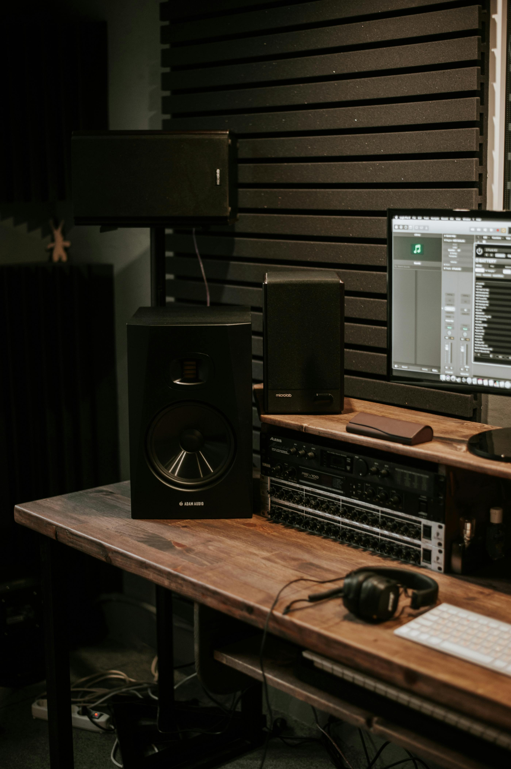 A modern audio studio setup featuring speakers, a computer, and headphones on a wooden desk.